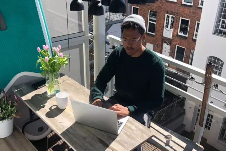 The young man with laptop is sitting on the balcony