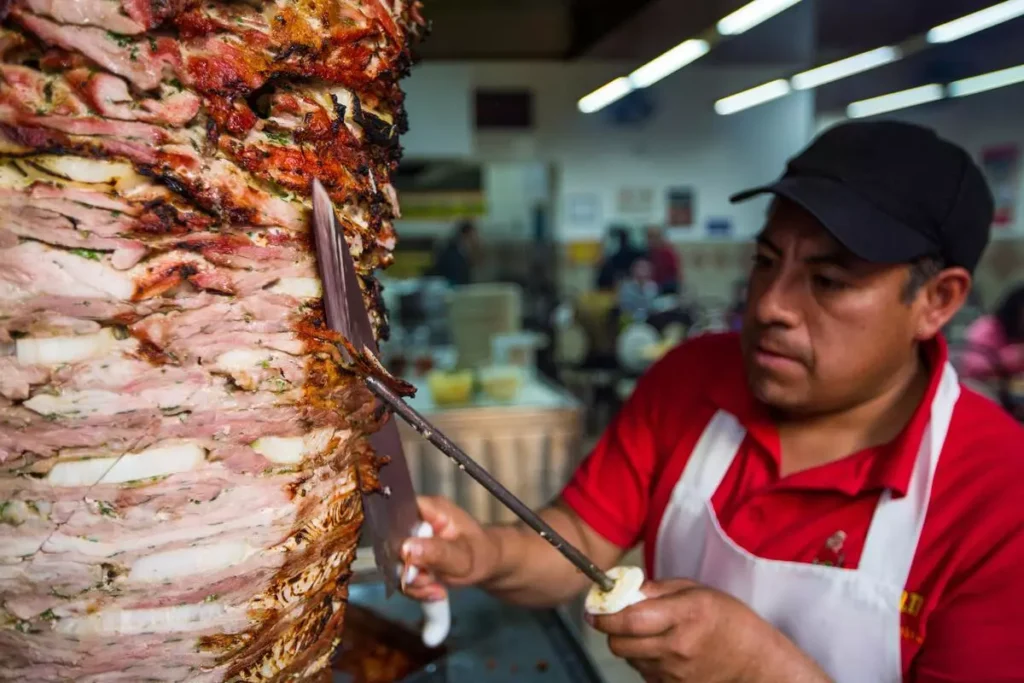 The Turkish man preparing slices the meat from a vertical spit.